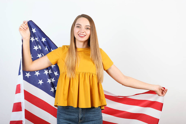 Beautiful young girl holding the flag of America on a colored background. - 写真・画像