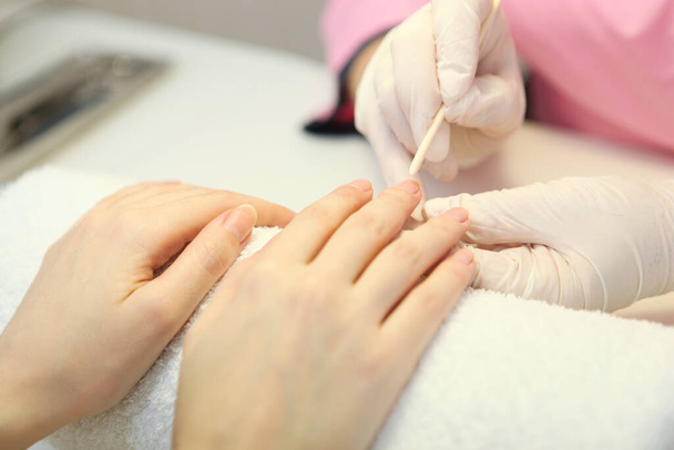 Een close-up van een vrouw in een nagelsalon die een manicure krijgt van een cosmetoloog met een nagelvijl. Een vrouw krijgt een manicure van nagels. Schoonheidsspecialiste zet nagels op de klant. - Foto, afbeelding