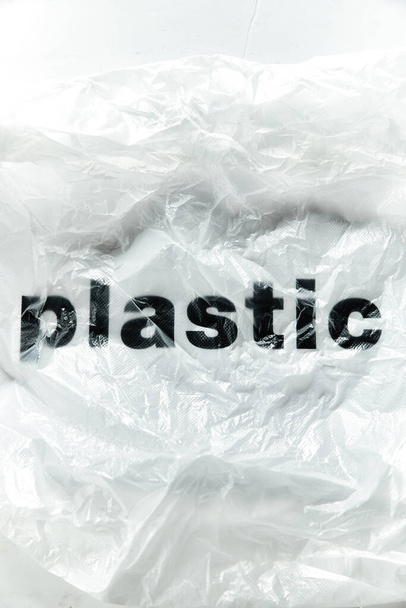 Černé plastové slovo na průhledném bílém jednorázovém plastovém sáčku. Obrázek konceptu znečištění životního prostředí s prostorem pro kopírování - Fotografie, Obrázek