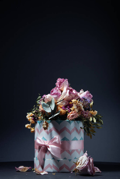 Strauß getrockneter Blumen in Geschenkbox auf dem Tisch vor dunklem Hintergrund - Foto, Bild