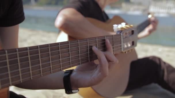 La mano de la mujer tocando la guitarra en la playa de arena, día soleado, de cerca
 - Metraje, vídeo