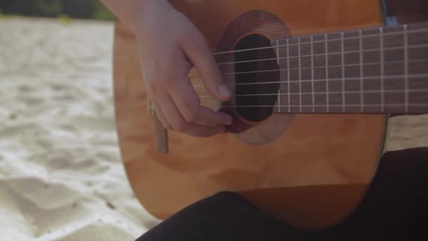 Γυναικείο χέρι χτυπά και παίζει κιθάρα στην αμμώδη παραλία, ηλιόλουστη μέρα, κοντινό πλάνο - Πλάνα, βίντεο