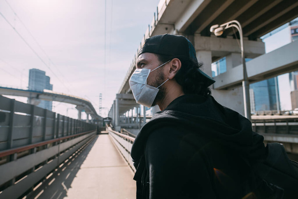 Un homme avec un masque médical sur un fond industriel. Jeune homme seul dans un masque sur un fond de routes vides et de passages supérieurs dans une métropole
 - Photo, image