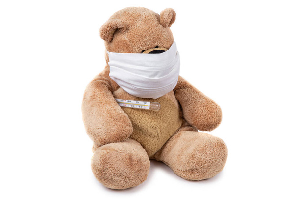 Der Teddybär sitzt krank mit Coronavirus in medizinischer Maske und Thermometer auf weißem Hintergrund. Bleiben Sie zu Hause. Kümmern Sie sich um Kinder. - Foto, Bild