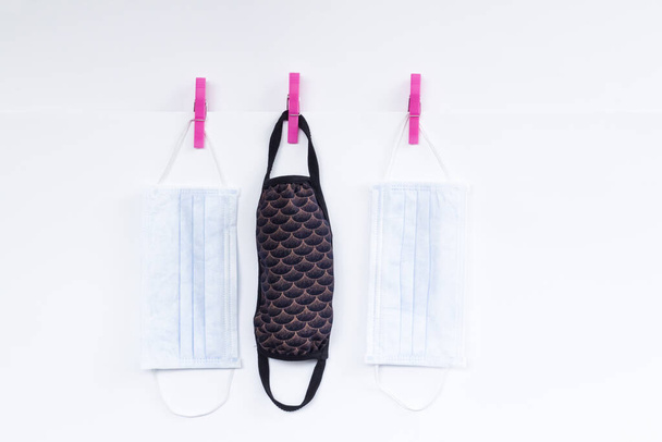 Handmade washable fabric face mask and surgical masks on white background hanging with laundry latch. - Fotó, kép