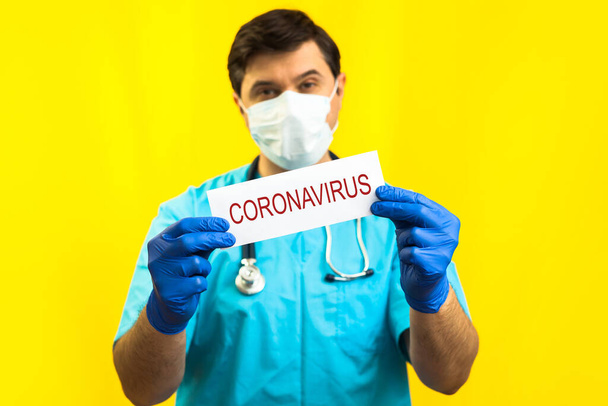 Koronavirüs karantinası kavramı. Roman Coronavirus 2019 NCoV. Sarı Arkaplan 'a karşı steteskoplu bir doktor elinde Coronavirus yazan beyaz bir kağıt tutuyor.. - Fotoğraf, Görsel