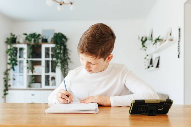 Hard-working school kid boy making homework math during quarantine time from corona pandemic disease. Education and distance learning for kids. Homeschooling during quarantine. Homeschooling concept - 写真・画像