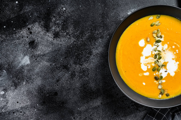 かぼちゃと人参のスープにクリームと調味料。黒の背景。最上階だ。スペースのコピー. - 写真・画像