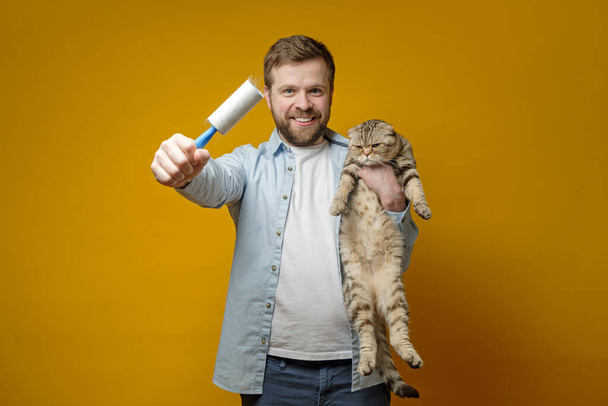 Tevreden, lachende man houdt in zijn hand een rol met duct tape in het haar van de dieren, in de andere knuffelt hij zijn geliefde kat. - Foto, afbeelding