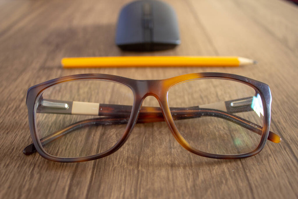 Крупный план по очкам с карандашом и мышью на заднем плане, на деревянном столе
 - Фото, изображение