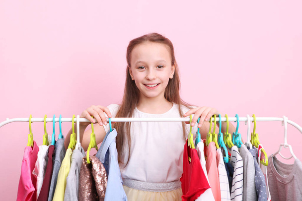 Schattig vrolijk meisje kiest kleren met vloerhangers. Kinderkleding, winkelen voor kinderen. Modieuze kleding voor kinderen. - Foto, afbeelding
