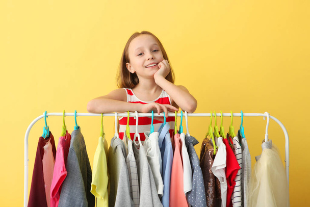 Cute cheerful little girl chooses clothes with floor hangers. Children's clothing, children's shopping. Fashionable clothes for children. - Photo, Image