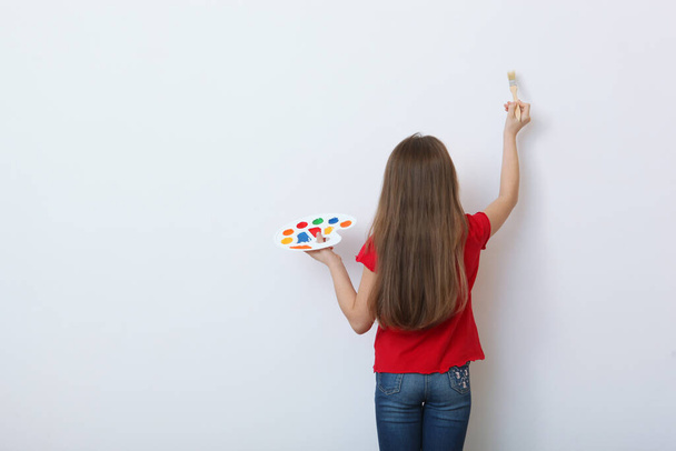 Cute happy girl with a palette for paints and a brush on a light background. - Photo, Image