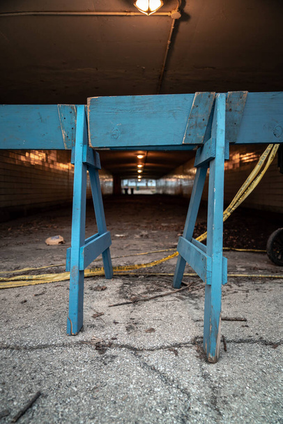 A view between two wooden legs to a blue police barricade and yellow police tape blocking the lakefront from public use during the COVID-19 pandemic and outbreak to help flatten the curve. - Photo, Image