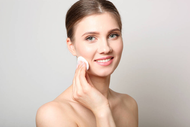 Portrait of a beautiful young girl with nude makeup on a light background who removes makeup with a cotton pad. The concept of healthy clean skin, spa, cosmetology. - Valokuva, kuva