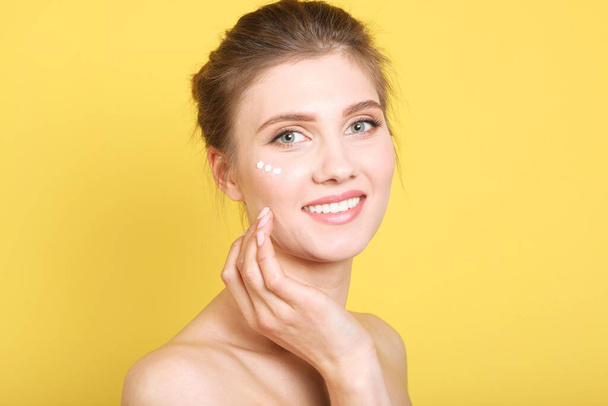 Portrait of a beautiful young girl on a colored background who uses caring cream. The concept of healthy clean skin, spa, skin care. - Photo, Image