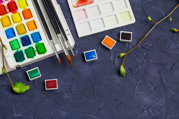Aquarelle und Pinsel auf dunklem Hintergrund, eine Palette heller Farben für kreatives Hobby und Selbstständigkeit - Foto, Bild