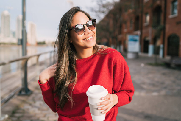 Portrait of beautiful young woman holding a cup of coffee outdoors. Urban concept. - Foto, Imagen
