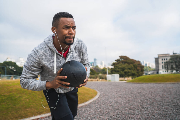Portrait of an athletic man training with medicine ball at the park outdoors. Sport and healthy concept. - Фото, изображение