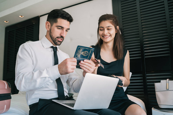 Portrait of two young business people buying flight tickets with laptop and credit card at hotel room. Business travel concept. - Photo, image
