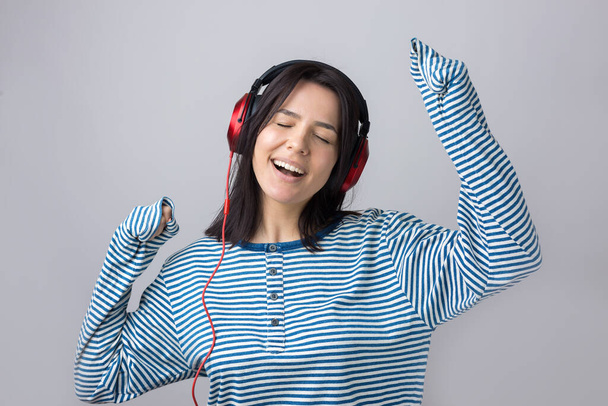 Una giovane ragazza con un gilet a righe sta ascoltando musica in cuffie rosse in uno studio e danza
. - Foto, immagini