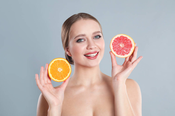 Young woman with cut orange and grapefruit on grey background. Vitamin rich food - Fotografie, Obrázek