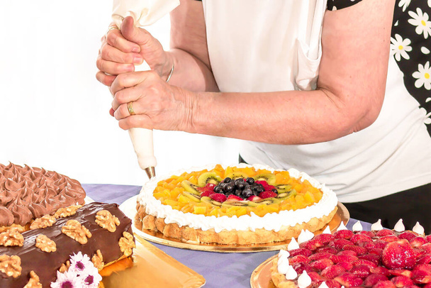 Készletkép egy felnőtt nőről, aki színes süteményeket dekorál tésztazsákkal - Fotó, kép