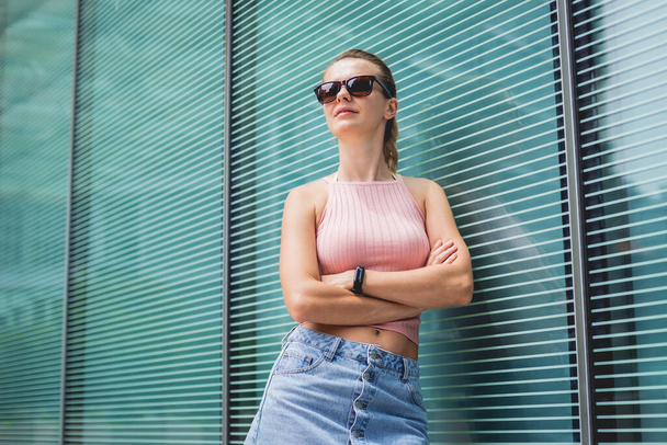 Young sexy woman in sunglasses posing near glass wall. - Φωτογραφία, εικόνα