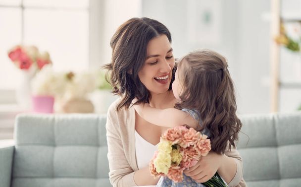 Happy mother's day! Child daughter congratulates mom and gives her flowers. Mum and girl smiling and hugging. Family holiday and togetherness.  - Foto, immagini