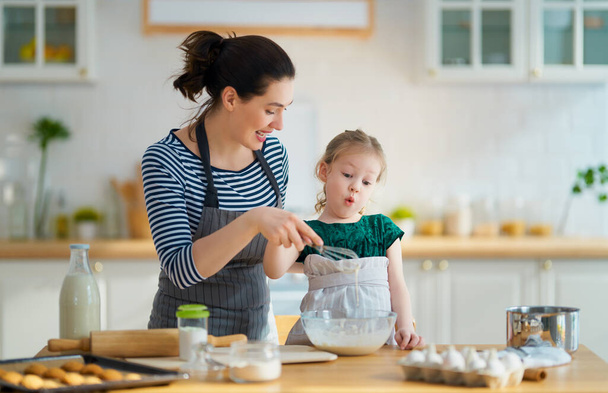 Happy loving family are preparing bakery together. Mother and child daughter girl are cooking cookies and having fun in the kitchen. Homemade food and little helper.                                 - Фото, изображение