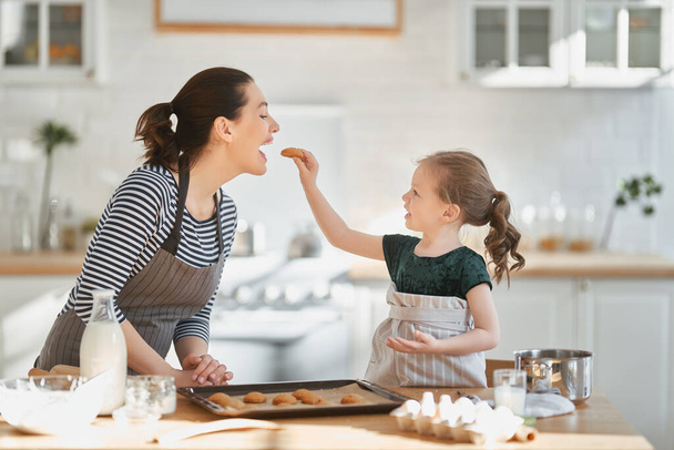 Šťastná milující rodina spolu připravuje pekárnu. Matka a dcera dcera dívka vaří sušenky a baví v kuchyni. Domácí jídlo a malý pomocník.                                 - Fotografie, Obrázek
