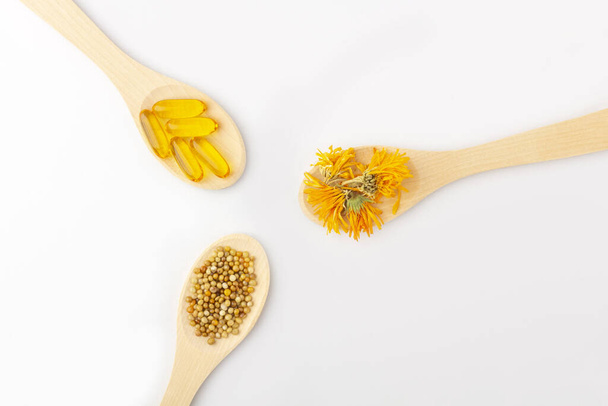 Herbal capsule, natural vitamins, dry calendula flowers at wooden spoon on white background. Concept of healthcare and alternative medicine: homeopathy and naturopathy. Close up, copy space for text - Photo, image