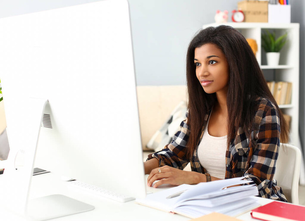 Donna nera sorridente seduta sul posto di lavoro che lavora con il PC desktop
 - Foto, immagini