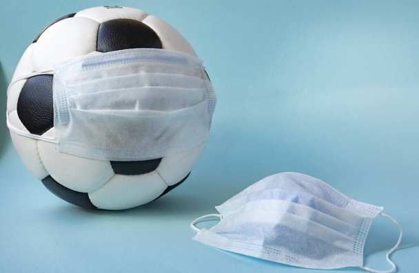 Soccer ball in a medical mask on a blue background.  Corona protection against viruses bacteria stop. Cancellation of sporting events.Copy space - Photo, Image