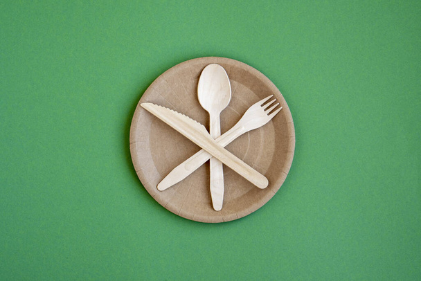Eco- friendly tableware for food and wooden ECO-knife, fork, spoon on a green background with a copy space. ECO-food packaging is made from recycled Kraft paper. ECO-friendly picnic dishes. Selective focus. - Photo, Image