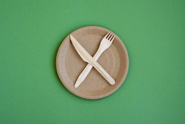 Eco- friendly tableware for food and wooden ECO-knife, fork, spoon on a green background with a copy space. ECO-food packaging is made from recycled Kraft paper. ECO-friendly picnic dishes. Selective focus. - Photo, image