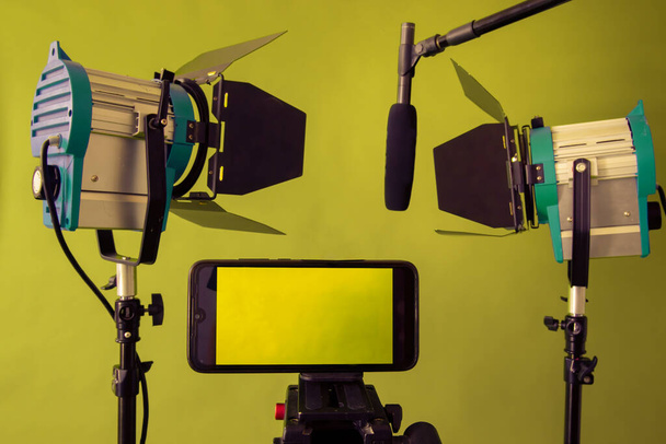 Live Stream Video Multimedia Concept. smartphone, μικρόφωνο και ανακλαστήρες στο πράσινο φόντο - Φωτογραφία, εικόνα