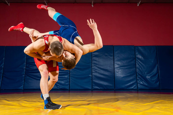 Two strong wrestlers in blue and red wrestling tights are wrestlng  on a wrestling carpet in the gym. Young man doing grapple. - Photo, Image