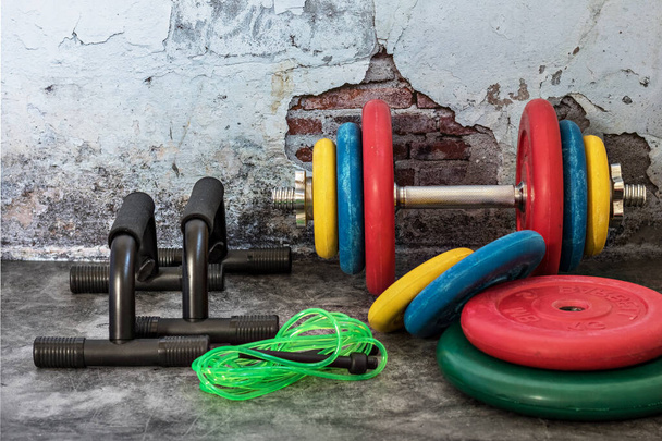 Professional dumbbells, multi-colored weight plates, jump rope and push-up stops on a vintage background. Sports equipment. Healthy lifestyle - Photo, Image
