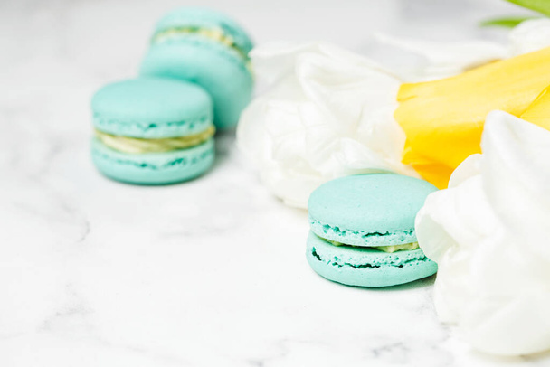 Macaroons closeup with white and yellow flowers on marble table. Mother's day concept - Photo, Image
