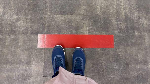 Persoon die op de tegelvloer staat met een rode lijn. Begrip afstand, sociale afstand, quarantaine of isolatie - Foto, afbeelding