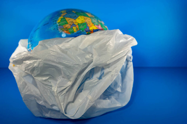 Grocery Plastic with earth inside with blue background. Earth is being destroyed because of too much garbage like plastic - Foto, Imagem