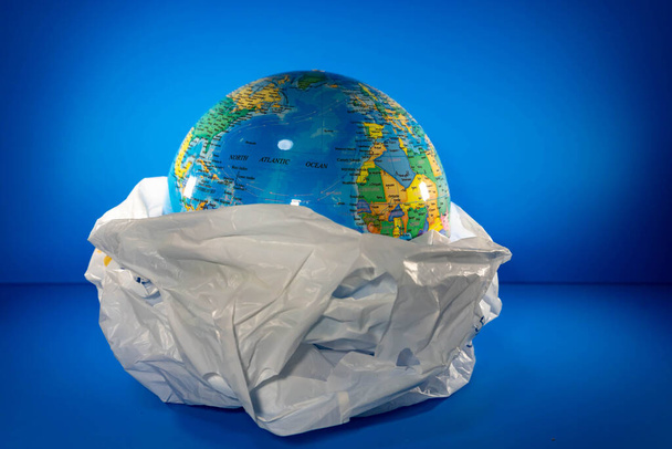 Παντοπωλείο Πλαστικό με χώμα στο εσωτερικό με μπλε φόντο. Η Γη καταστρέφεται εξαιτίας πολλών σκουπιδιών όπως τα πλαστικά. - Φωτογραφία, εικόνα