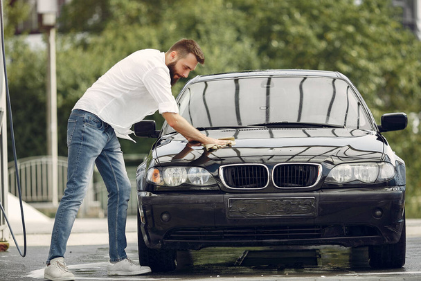 Man in a white shirt wipes a car in a car wash - Foto, Imagen