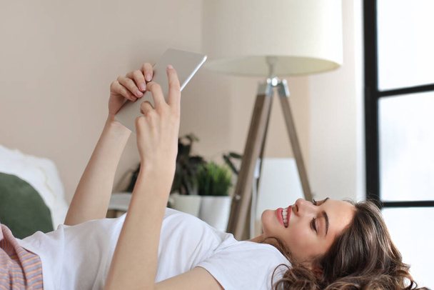 Uśmiechnięta kobieta leży na łóżku i używa tabletu cyfrowego - Zdjęcie, obraz