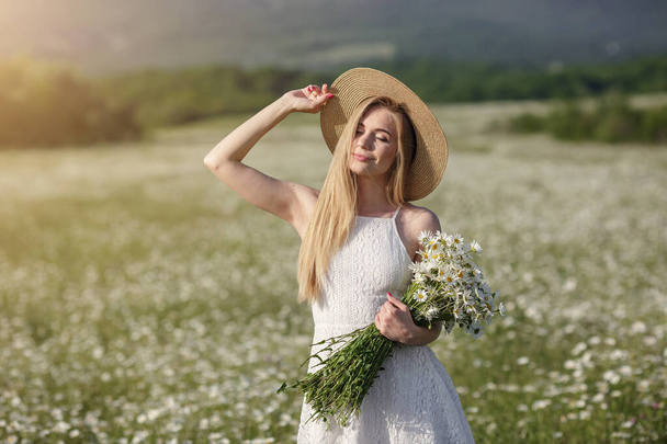 beautiful young woman in a camomile field in a picturesque valley. happy young lady and spring green nature, harmony concept. the idea of self-care, a healthy lifestyle and a positive attitude - Foto, Imagem
