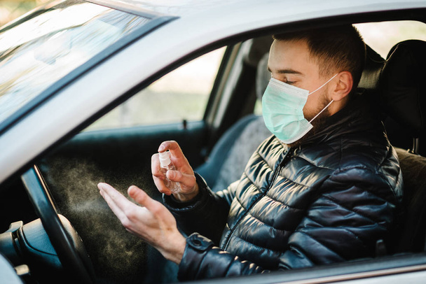 Spraying anti-bacterial sanitizer spray on hand in car, infection control concept. Sanitizer to prevent Coronavirus, Covid-19, flu. Spray bottle. Man wearing in medical protective mask driving a car. - Foto, immagini