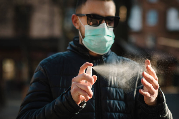 Coronavirus. Cleaning hands with sanitizer spray in city. Man wearing in medical protective mask on street. Sanitizer to prevent Coronavirus, Covid-19, flu. Spray bottle. Virus and illness protection. - Photo, image