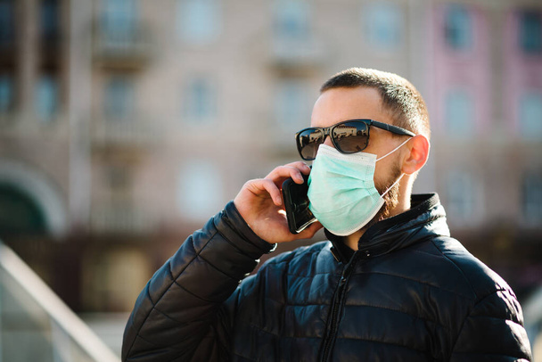 Coronavirus. Man wearing medical protective mask and talking on cell mobile phone, walking on street. Prevent Covid-19, flu. Feeling bad in city. Person needs help. Virus, pandemic, panic concept. - Foto, imagen