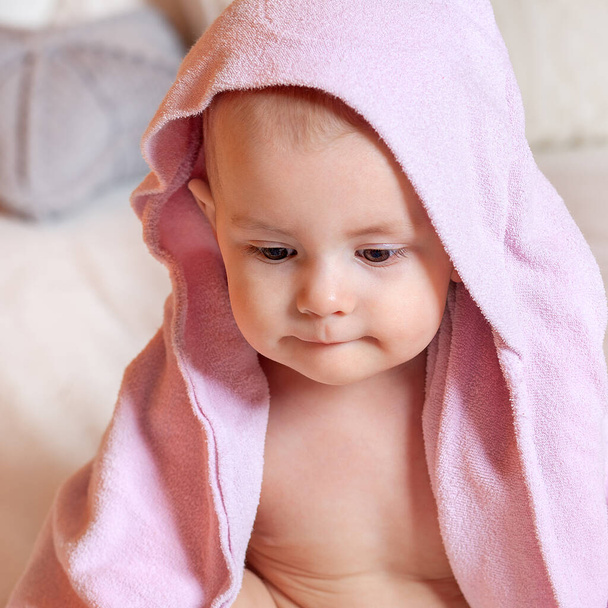 Touching portrait of a one-year-old baby after bathing. Nice face with pursed lips. Textiles and bedding for children. Pink bath towel. - Foto, afbeelding